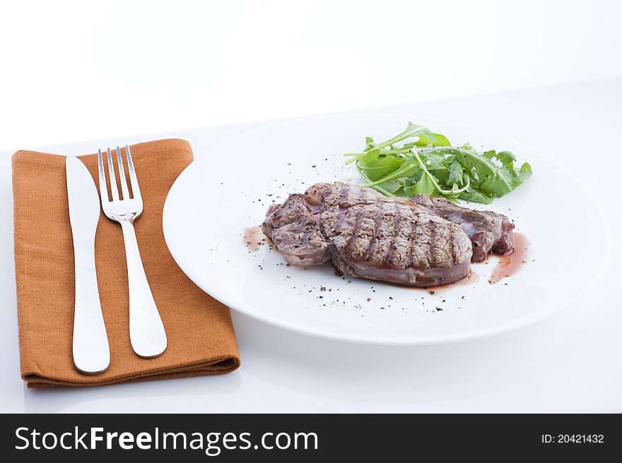 Grilled beef, served with arugula on a plate, view of the table with a white background