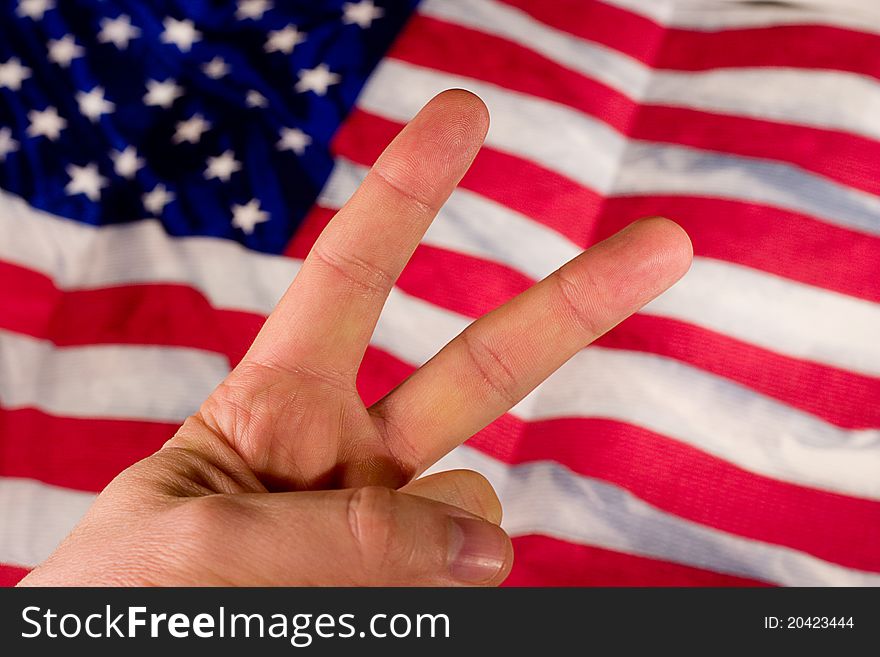 A hand holds up a peace sign in front of an American Flag. A hand holds up a peace sign in front of an American Flag.