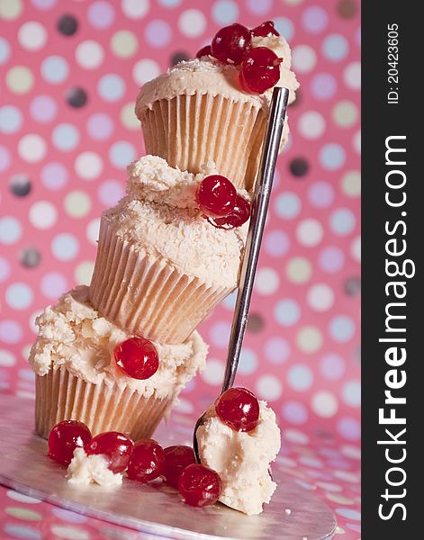 Stacked cupcakes with icing and glacé cherries and fun polka dot background. Stacked cupcakes with icing and glacé cherries and fun polka dot background