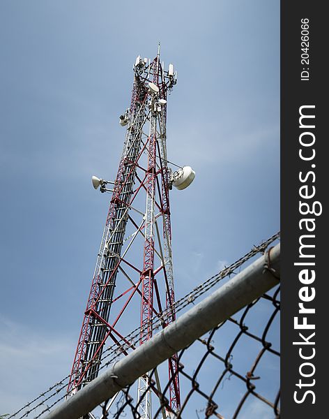 Radio communication tower against blue sky behind chain link fence and barbed wire. Radio communication tower against blue sky behind chain link fence and barbed wire