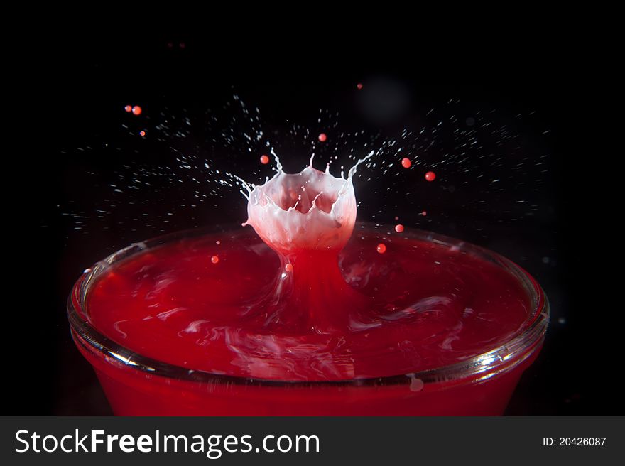 A high-speed photo of a 2 drops of cream falling into a bowl of red tinted water. A high-speed photo of a 2 drops of cream falling into a bowl of red tinted water.