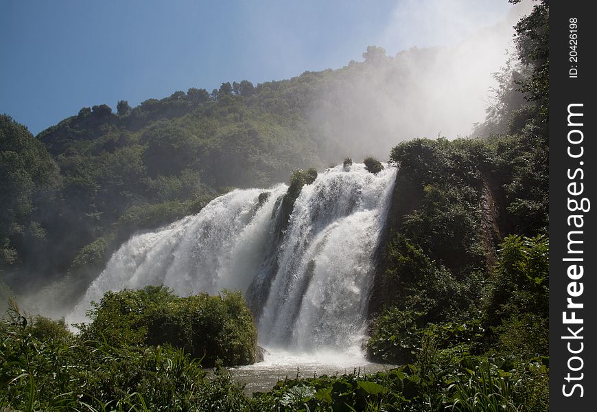 Lower view of Marmore waterfalls surrounded by green grass and trees. Lower view of Marmore waterfalls surrounded by green grass and trees