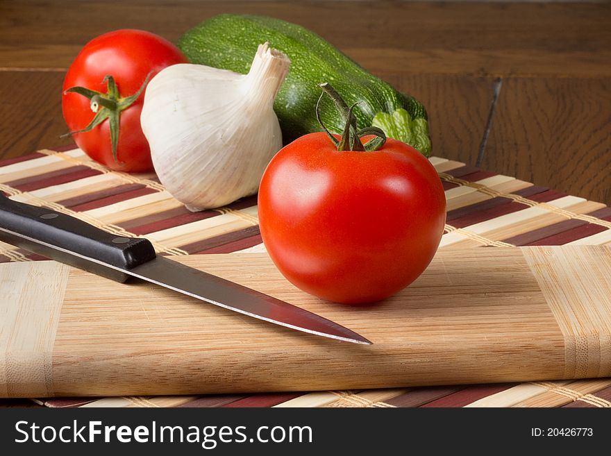 Fresh tomato, garlic and zucchini on a cutting board ready to be sliced