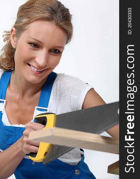 Woman wearing blue overalls sawing plank of wood. Woman wearing blue overalls sawing plank of wood