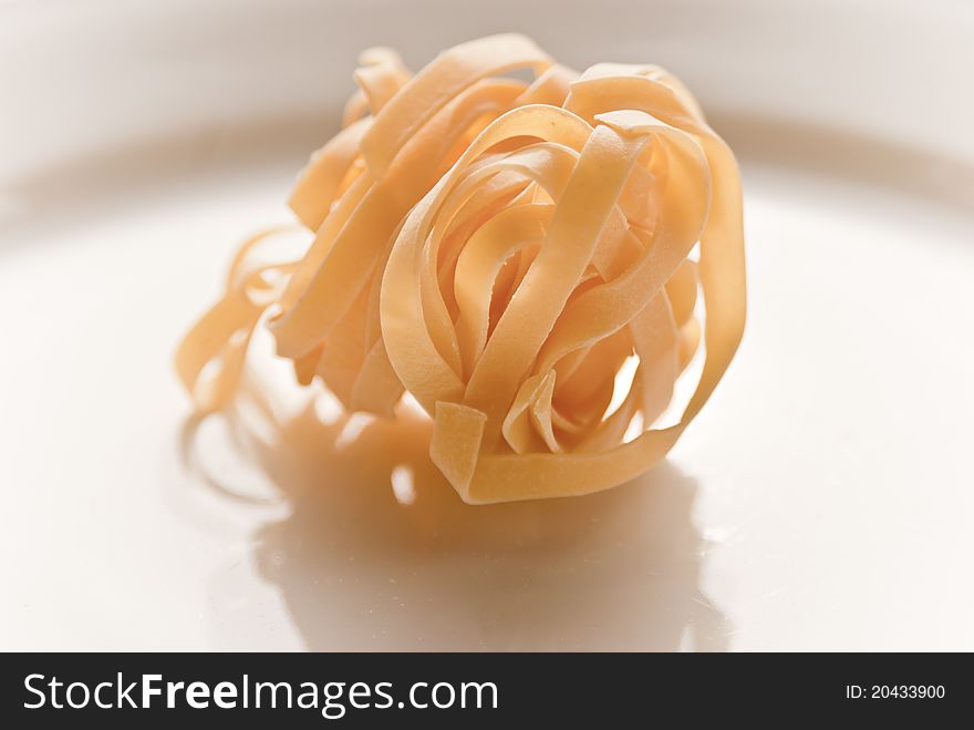 A plate of dried tagliatelle pasta shot in natural sunlight on a white plate