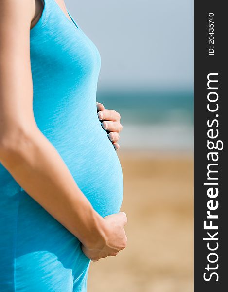 Woman is holding pregnant belly on the beach