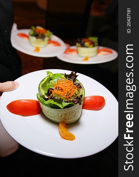 Fancy appetizer salad on white plate. Small green/colorful salad in circular design.