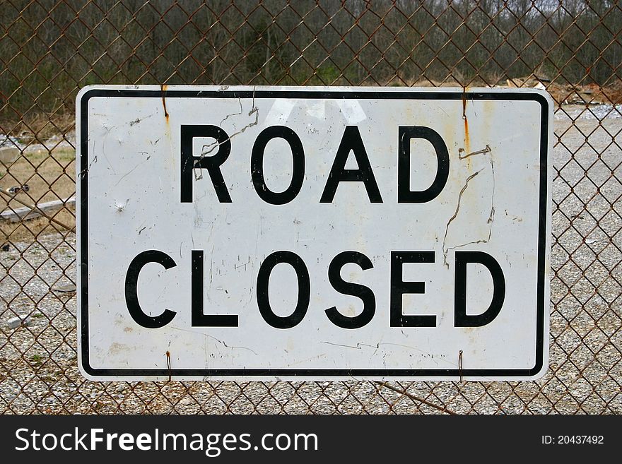 A road closed sign fastened to a chain link fence