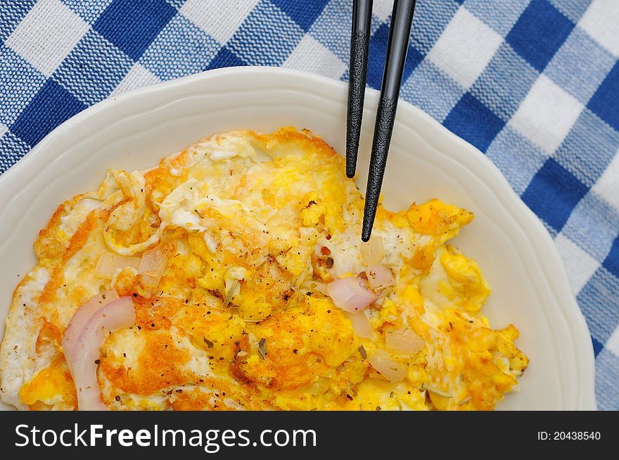 Onion fried egg on white plate with chopsticks.