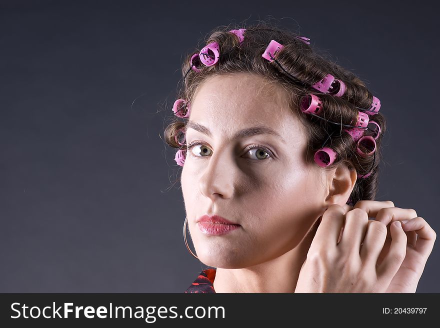 Portrait of a young beautiful woman with bigoudi on the hair on a gray background closeup. Portrait of a young beautiful woman with bigoudi on the hair on a gray background closeup