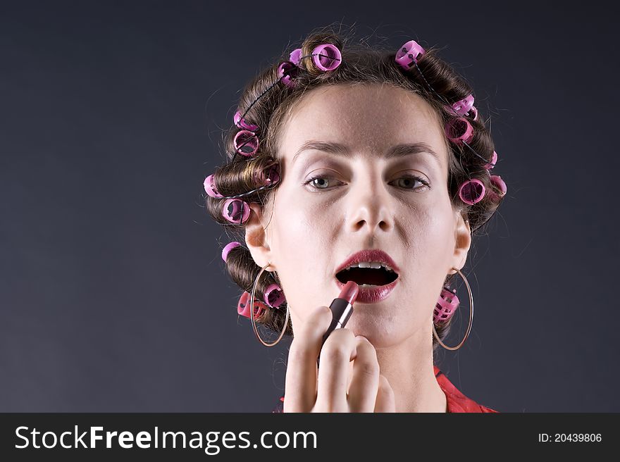 Beautiful girl in a red robe home paints her lips on a gray background closeup