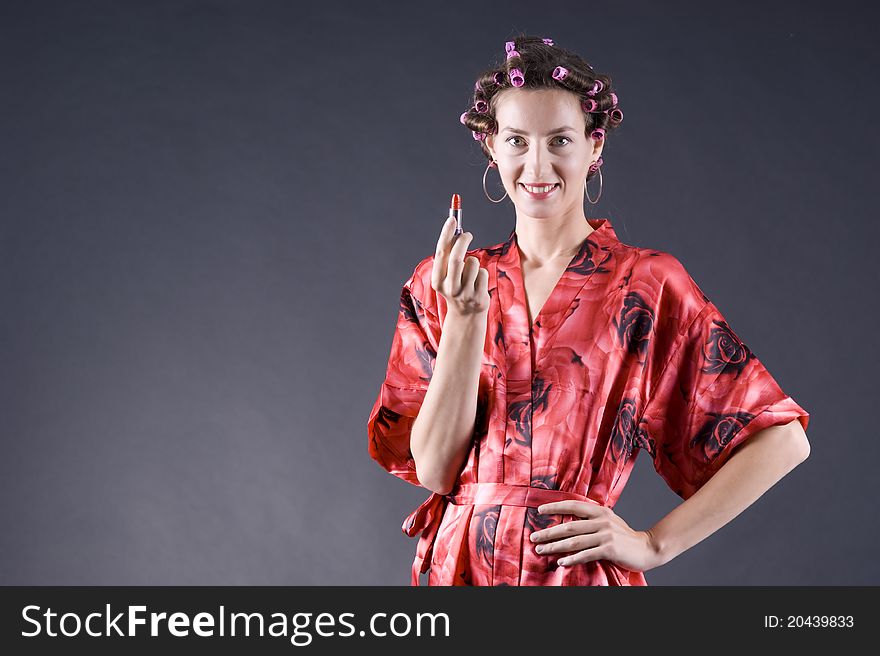 Beautiful girl in a red robe home paints her lips on a gray background closeup