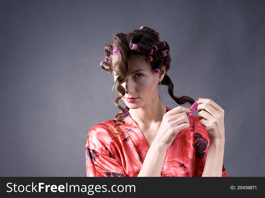 Portrait of a  young beautiful woman with bigoudi on the hair on a gray background closeup. Portrait of a  young beautiful woman with bigoudi on the hair on a gray background closeup