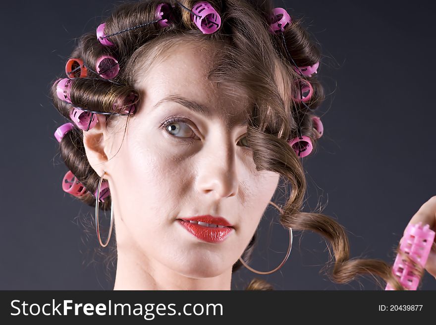 Portrait of a young beautiful woman with bigoudi on the hair on a gray background closeup. Portrait of a young beautiful woman with bigoudi on the hair on a gray background closeup