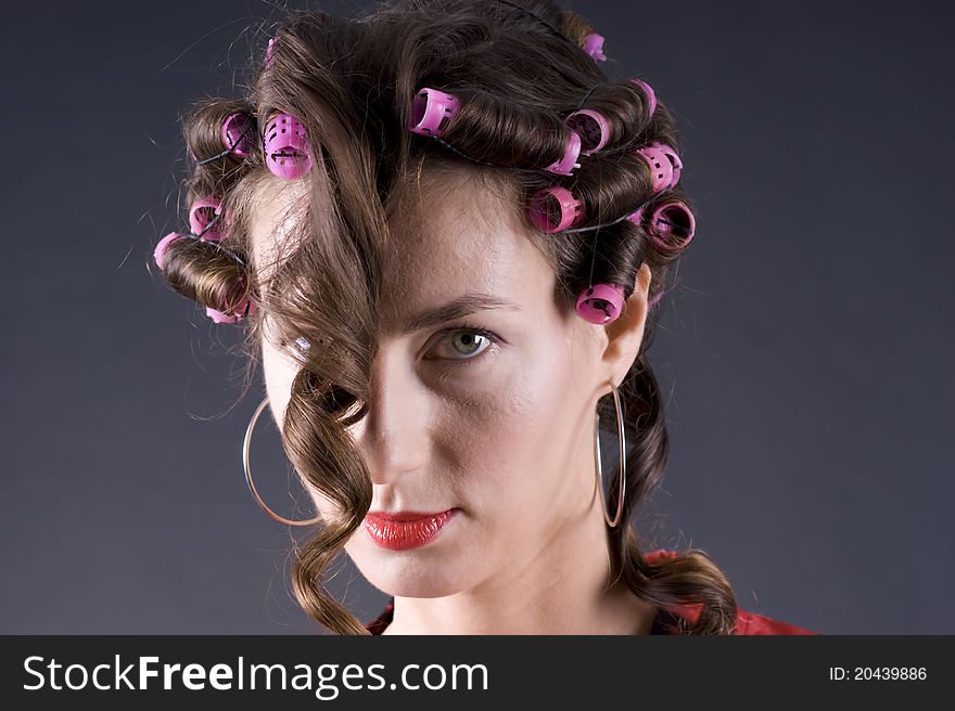 Portrait of a  young beautiful woman with bigoudi on the hair on a gray background closeup. Portrait of a  young beautiful woman with bigoudi on the hair on a gray background closeup