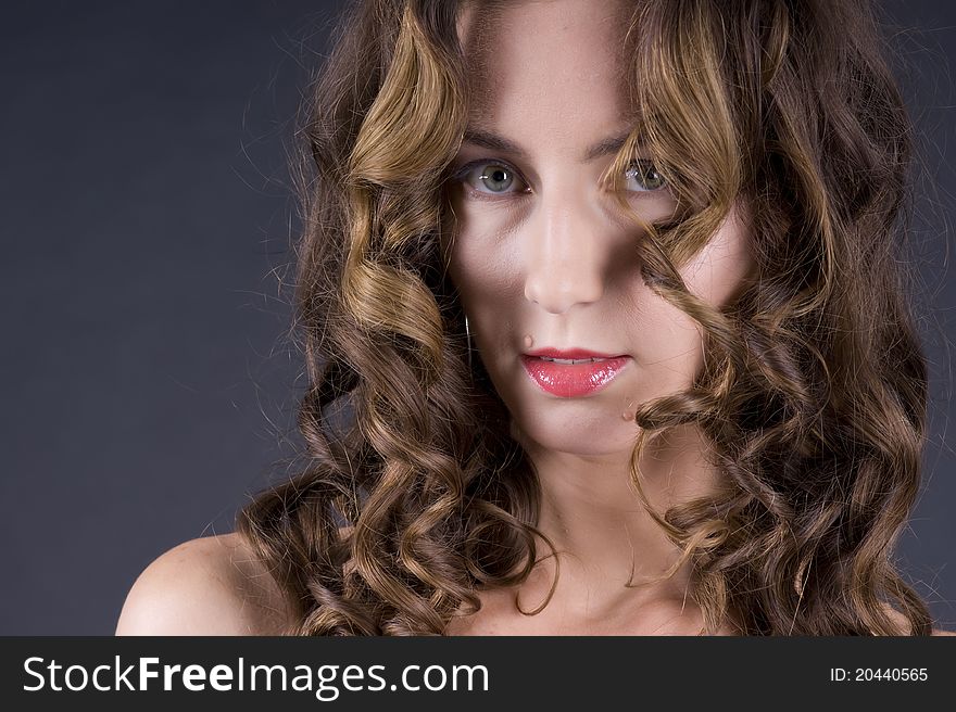 Portrait of a young beautiful woman with long wavy hair on a gray background closeup. Portrait of a young beautiful woman with long wavy hair on a gray background closeup