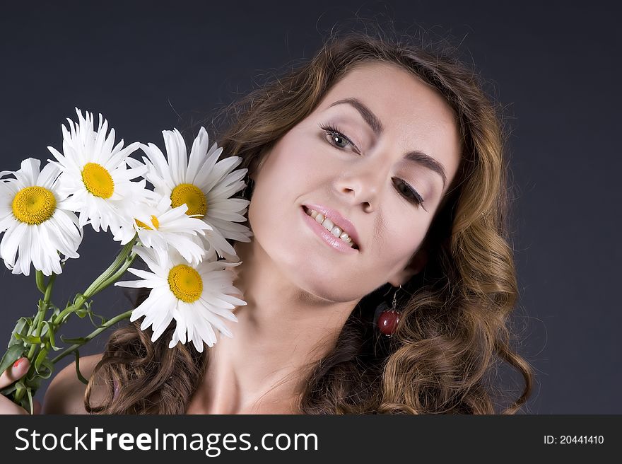 Portrait of a young beautiful woman with camomile on a gray background closeup. Portrait of a young beautiful woman with camomile on a gray background closeup