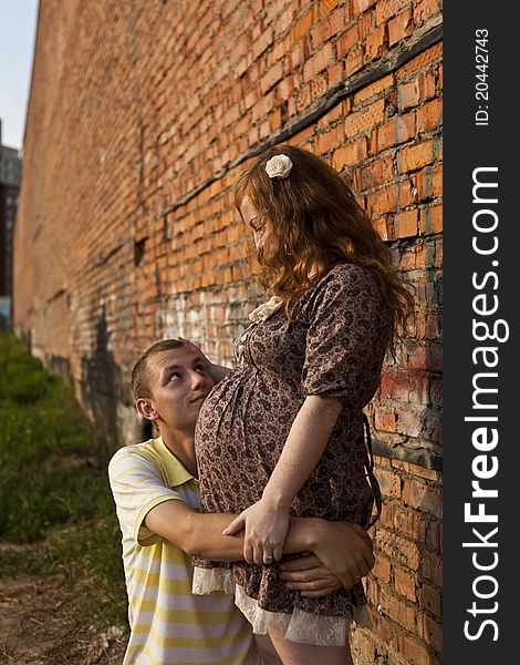 Portrait of a happy young man kisses his pregnant wife . outdoor .