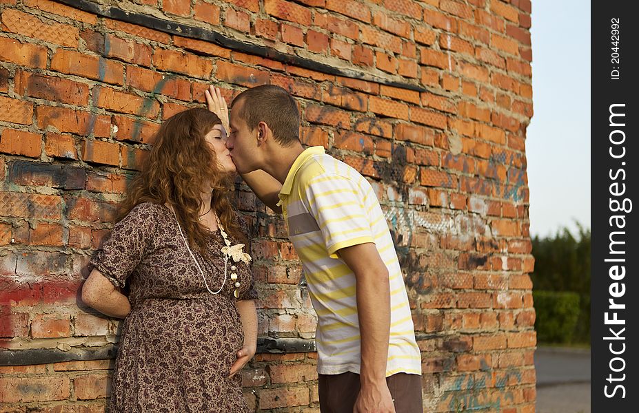 Portrait of a happy young man kisses his pregnant wife . outdoor .