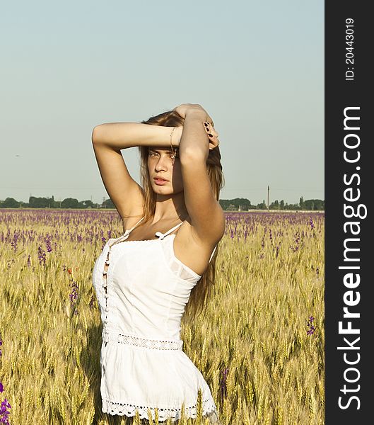 The red-haired girl among wheat ears in beams of the sunset