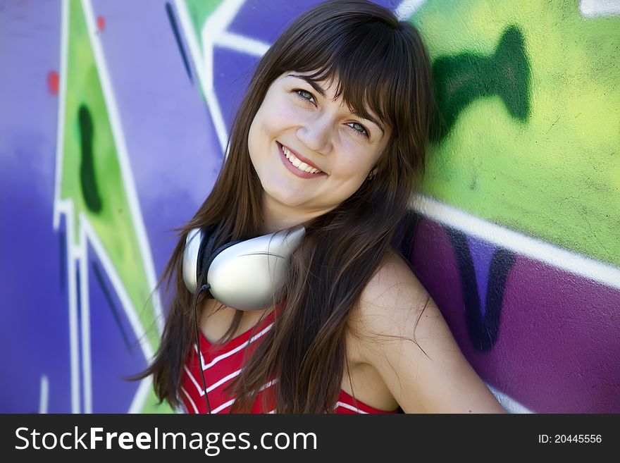 Beautiful brunette girl with headphones and graffiti wall at background.