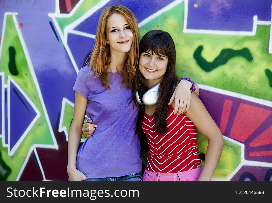 Two girlfriends near graffiti wall.