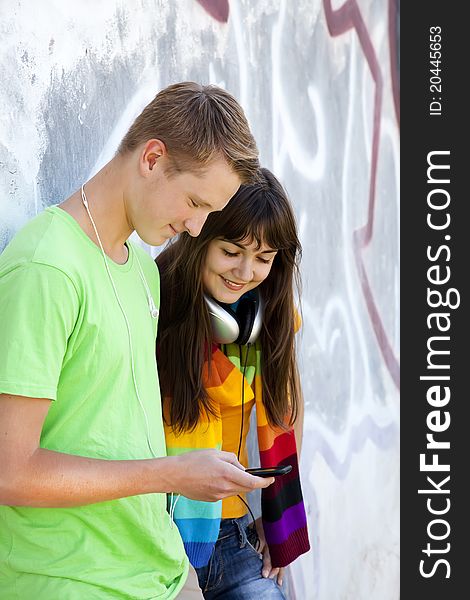 Teens with headphones near graffiti wall.