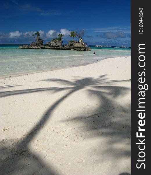 Lovely palm tree shadows sneaking along a white sand beach with inviting turquoise waters right behind - and a tiny, palm tree covered rock island begging to be explored. Taken on Boracay island, The Philippines. Lovely palm tree shadows sneaking along a white sand beach with inviting turquoise waters right behind - and a tiny, palm tree covered rock island begging to be explored. Taken on Boracay island, The Philippines.