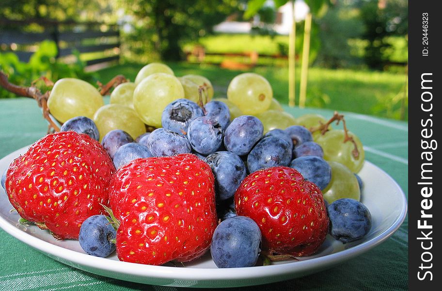 Delicious and Healthy Fruit Plate including strawberries, blueberries and grapes, served on the garden terrace on a sunny summer day. Hmmm... Just bite!