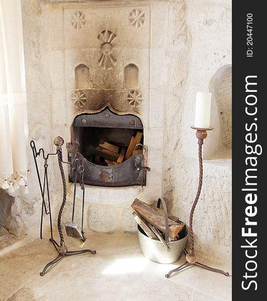 Corner fireplace in a cave room with detailing on chimney with tools, logas, candle in a brass stand ad alcove. Corner fireplace in a cave room with detailing on chimney with tools, logas, candle in a brass stand ad alcove