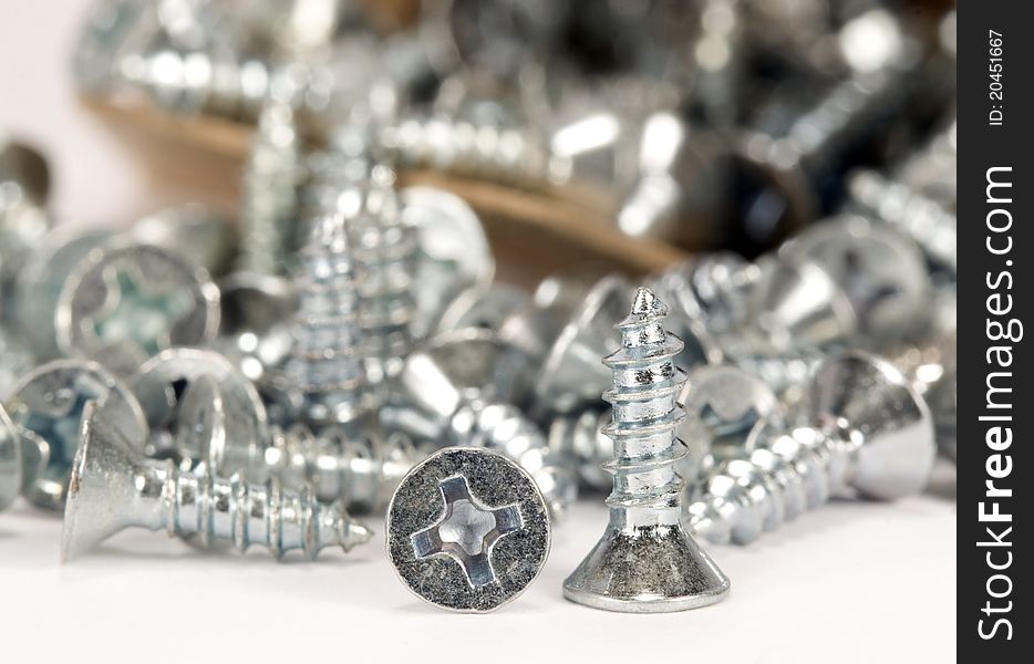 Flat head wood screws, one standing on head, one on side with phillips head showing, one lying on side and additional screws  spilling out of box softly blurred in background. Flat head wood screws, one standing on head, one on side with phillips head showing, one lying on side and additional screws  spilling out of box softly blurred in background