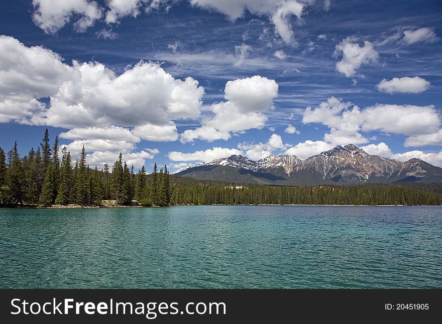 Lake Beauvert in Jasper National Park on a beautiful sunny day. Turquoise water and bright blue sky with puffy white clouds. Pyramid Mountain is in the distance.