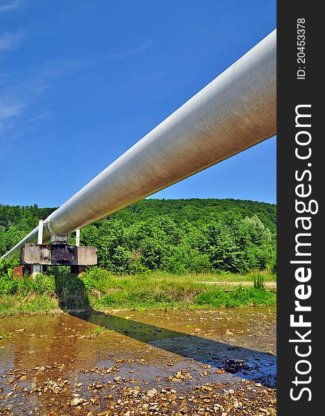 The high pressure pipeline in a summer landscape with the dark blue sky and clouds.