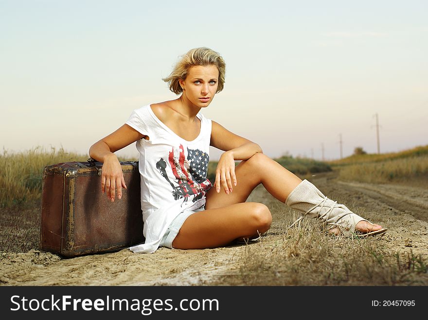 Pretty girl sitting on a suitcase on a countryside road