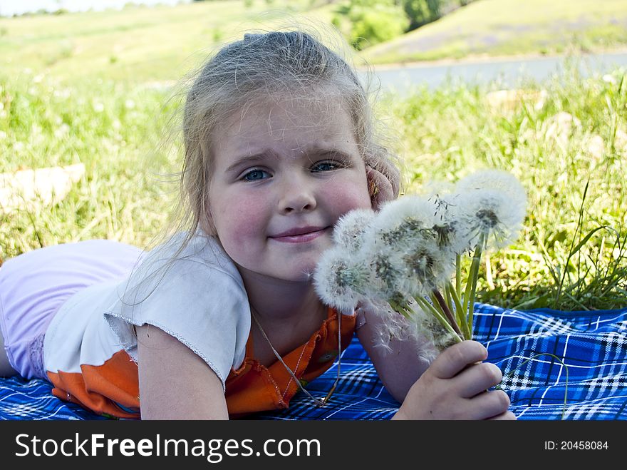 The girl lays on a meadow and holds in hands a bouquet from dandelions. The girl lays on a meadow and holds in hands a bouquet from dandelions