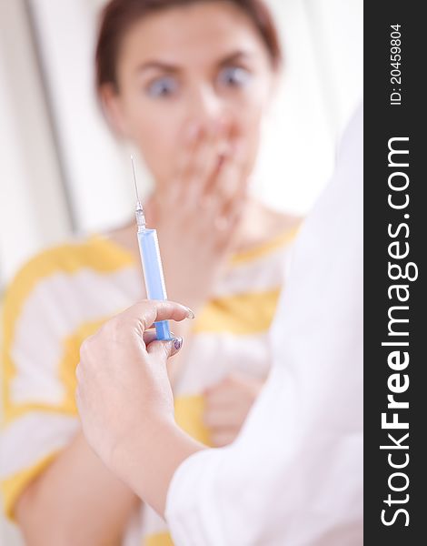Doctor preparing vaccination injection - patient in fear on background. Focus on syringe and hand. Doctor preparing vaccination injection - patient in fear on background. Focus on syringe and hand.