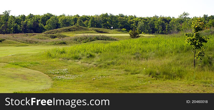 Golf green showing flag pole and green side bunker. In the background is an the next holeâ€™s tee box. The golf course is an old world links style course. Golf green showing flag pole and green side bunker. In the background is an the next holeâ€™s tee box. The golf course is an old world links style course.