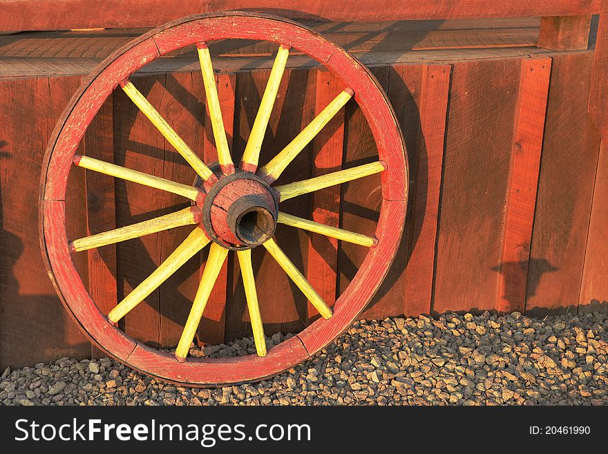 A colorful red and yellow antique wagon wheel leaning against a redwood porch