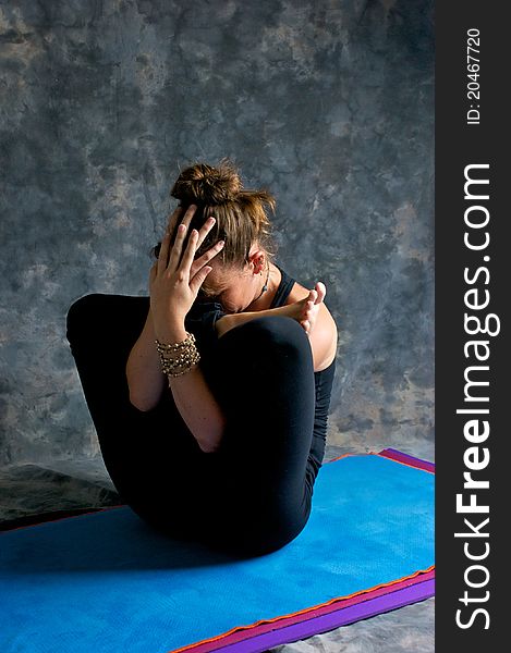 A brown haired caucasian woman is doing yoga exercise, Womb Embryo Posture or Garbha Pindasana posture studio on yoga mat with grey mottled background. A brown haired caucasian woman is doing yoga exercise, Womb Embryo Posture or Garbha Pindasana posture studio on yoga mat with grey mottled background.