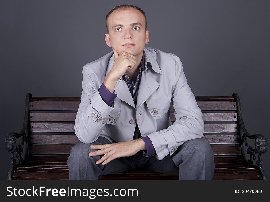 A man in a gray cloak  sits on a street bench brown