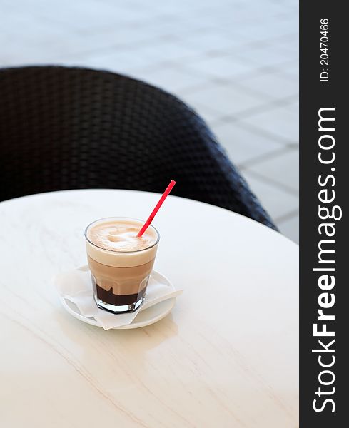 Glass of cappuccino standing on ring table near chair. Glass of cappuccino standing on ring table near chair