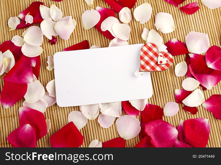 At the rose petals is white piece of paper and a red heart. Postcard. At the rose petals is white piece of paper and a red heart. Postcard