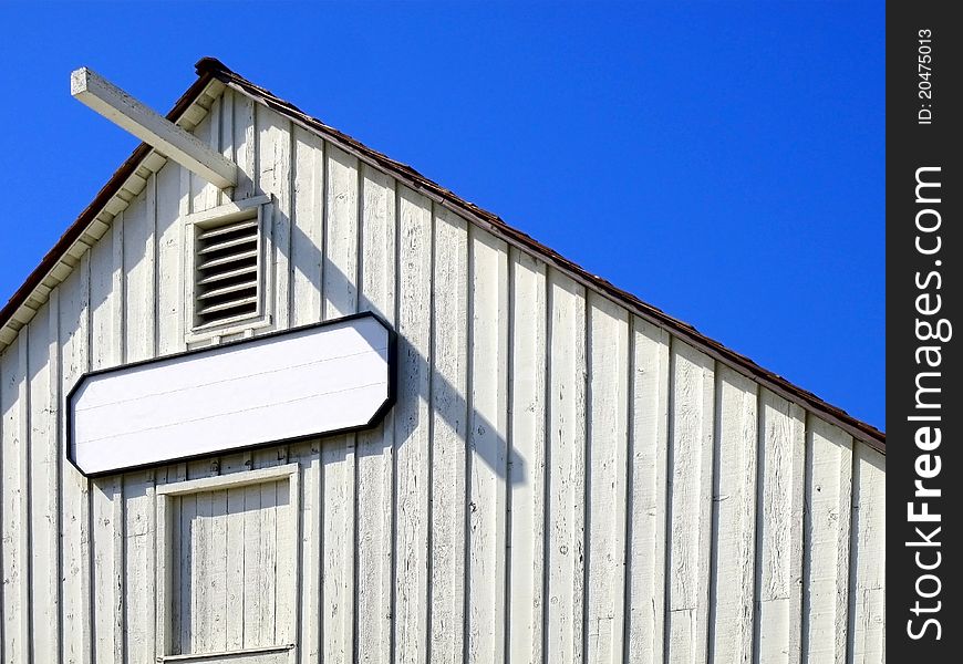 Old white barn with blue sky and blank sign that is ready to fill in with any words