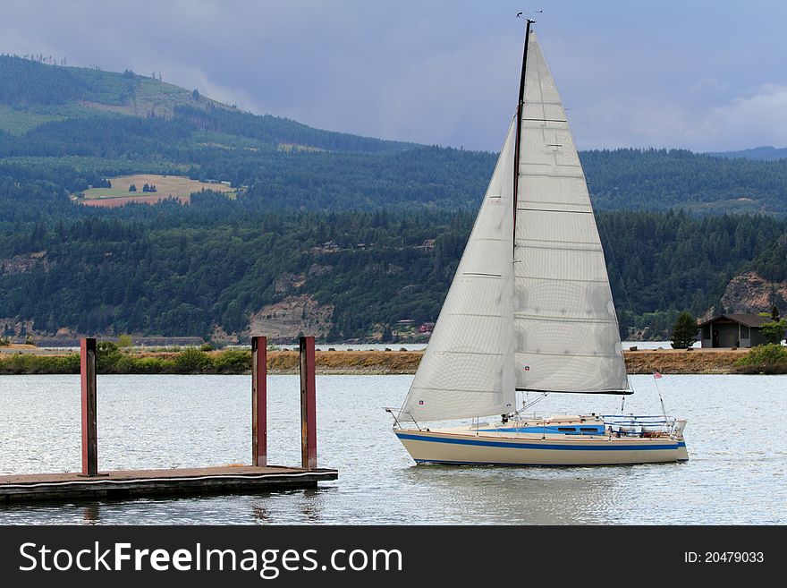 A sailboat by a dock, cloudy skies, view of territory.