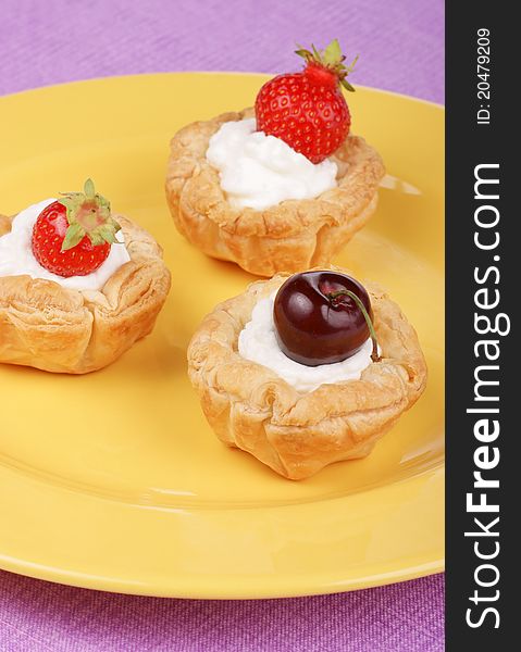 Small tarts with whipped cream, strawberries and cherries served on a yellow plate. Small tarts with whipped cream, strawberries and cherries served on a yellow plate