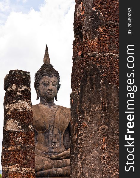 Ruin Buddha statue behind ruin pillars in Sukhothai historic park. Ruin Buddha statue behind ruin pillars in Sukhothai historic park