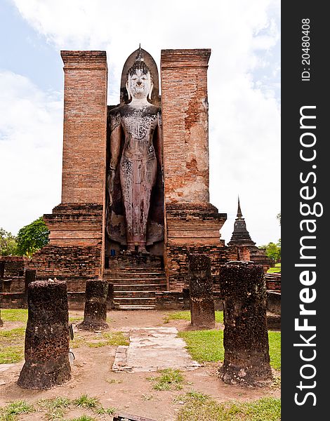 Ruin standing Buddha statue behind pillars in Sukhothai historic park vertical. Ruin standing Buddha statue behind pillars in Sukhothai historic park vertical