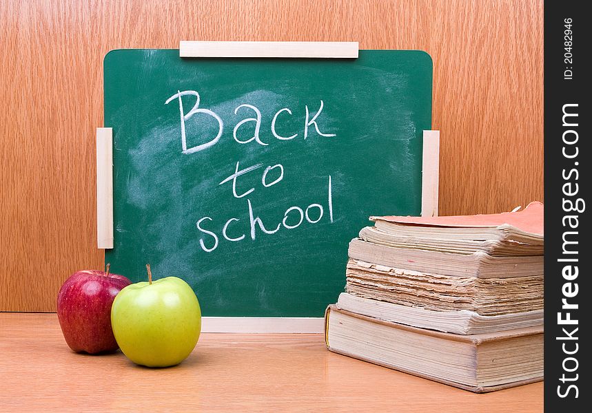 Back to school written on board with books and apples on the wooden table. Back to school written on board with books and apples on the wooden table