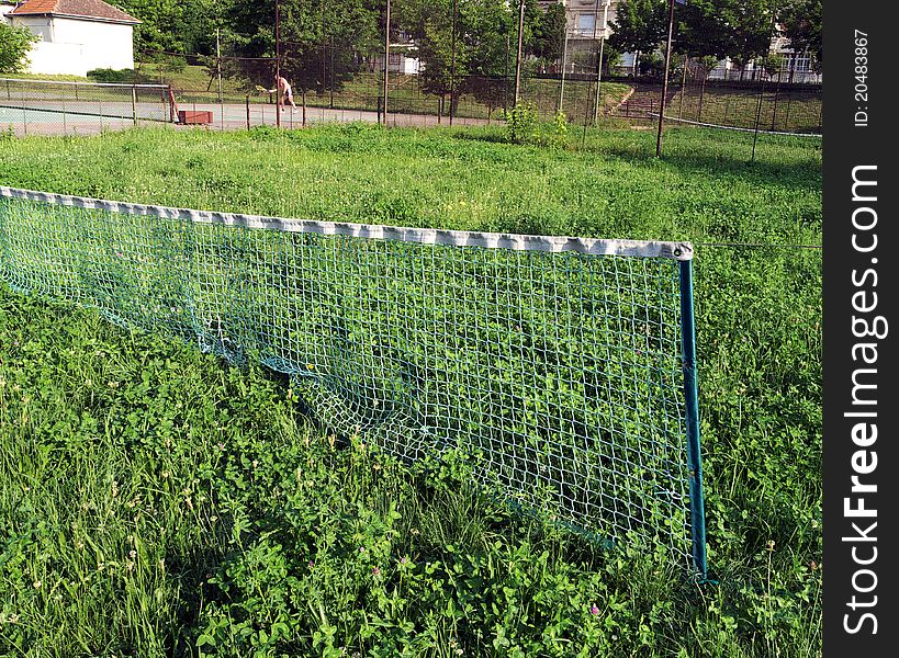 An abandoned tennis court where weeds grew on top of the grass. The net is still there waiting for better days