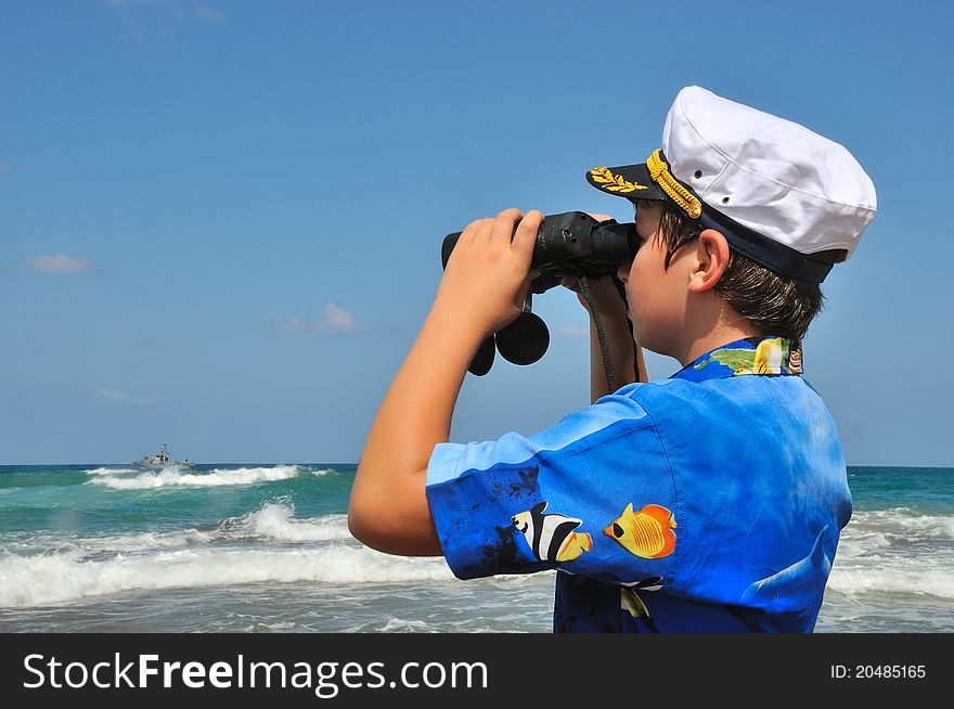 The Boy in the naval cap, considering the ship with binoculars who sailed to sea. The Boy in the naval cap, considering the ship with binoculars who sailed to sea